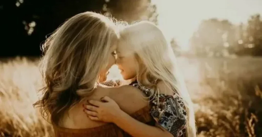 Mother and daughter embracing forehead to forehead in golden sunset field