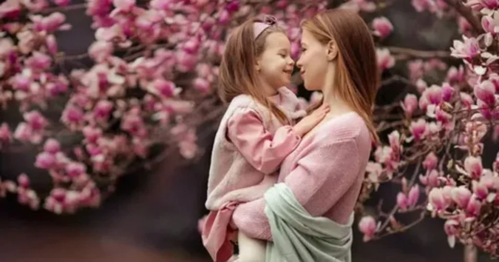 Mother holding daughter face to face among pink blossom flowers